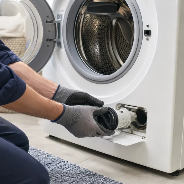 Washer Repair service photo. Technician inspecting the drain-pump filter on a front-load washing machine.